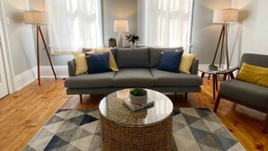 Ein Wohnzimmer mit grauem Sofa, zwei Sesseln, einem Couchtisch und zwei Stehlampen.