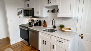 A modern kitchen with white cabinetry, stainless steel appliances, and a wooden floor. - Explore Downtown and Mount Adams with River Views! (Cincinnati)