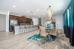 A modern kitchen with stainless steel appliances, a central island with bar seating, and a dining area with a chandelier.