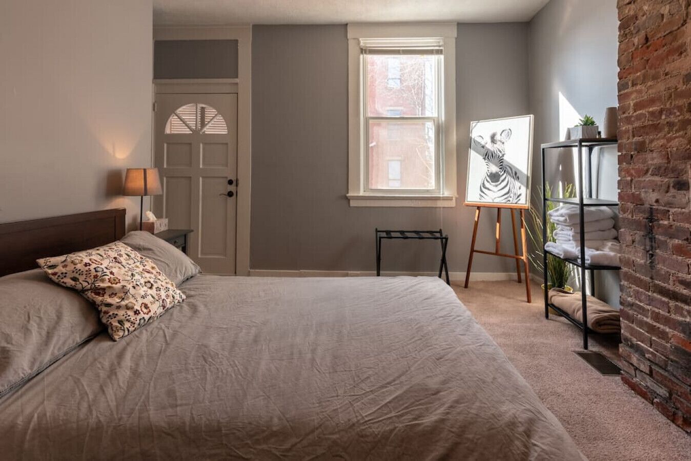 A bedroom with a bed, a door, a window, and a brick wall.