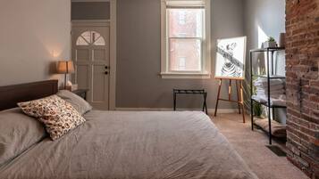 A bedroom with a bed, a door, a window, and a brick wall.