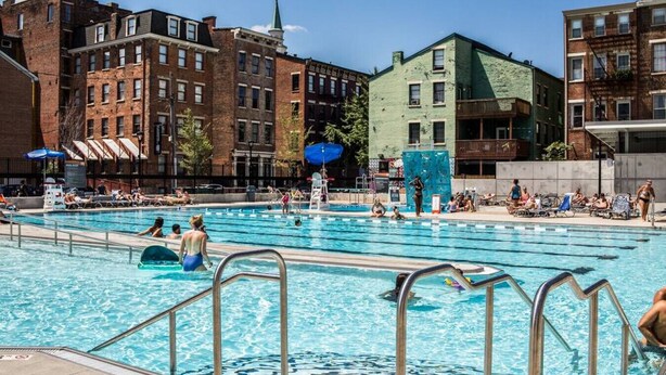 Piscina pública com várias pistas de natação, rodeada por edifícios urbanos.