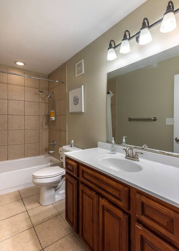 A bathroom with a bathtub, toilet, and vanity with a large mirror.