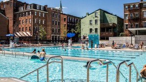 A public swimming pool with multiple lanes, surrounded by multi-story buildings with brick facades.