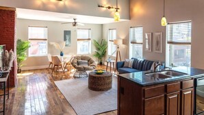 A spacious living room with a wooden floor, a sofa, a dining area, and a kitchen with a large island.