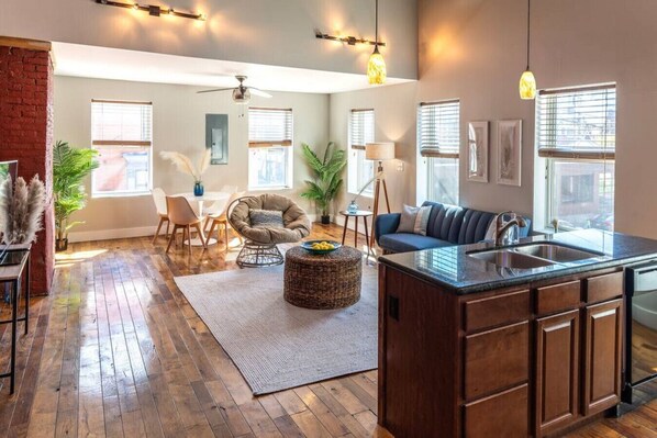 A spacious living room with a wooden floor, a sofa, a dining area, and a kitchen with a large island.