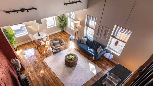 A spacious living room with a large window, a blue sofa, a round coffee table, and a kitchen area with a sink.