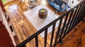 A spacious loft with high ceilings, a wooden floor, a blue sofa, a round ottoman, and a dining area with a white table and chairs.