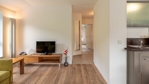 A modern living room with a flat-screen TV, wooden furniture, and a vase with flowers. - Apartment Glacier View 14.6. with balcony (Kaprun)