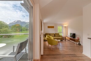 A modern living room with a sofa, yellow armchair, and a TV on a wooden console. A glass door leads to a balcony with a mountain view. - Apartment Glacier View 14.6. with balcony (Kaprun)
