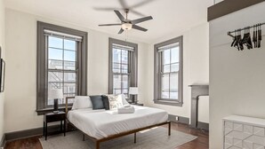 Une chambre à coucher avec un lit, des tables de chevet, un ventilateur de plafond et une cheminée.