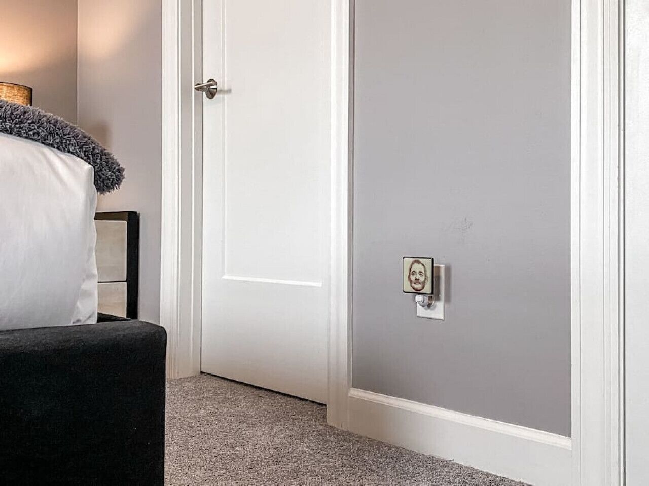 A room with a white door, a grey wall, and a small picture frame on the wall.
