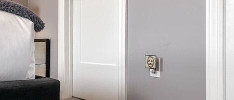 A room with a white door, a grey wall, and a small picture frame on the wall.