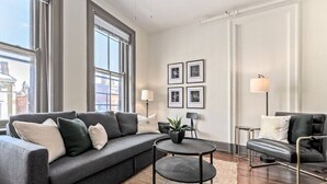 A modern living room with a grey sofa, a round coffee table, and a black armchair. There are framed pictures on the wall and a floor lamp. - Deluxe 5-bedroom Condo Walkable to Everything (Cincinnati)
