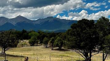 Paisaje rural con montañas, árboles y animales pastando.