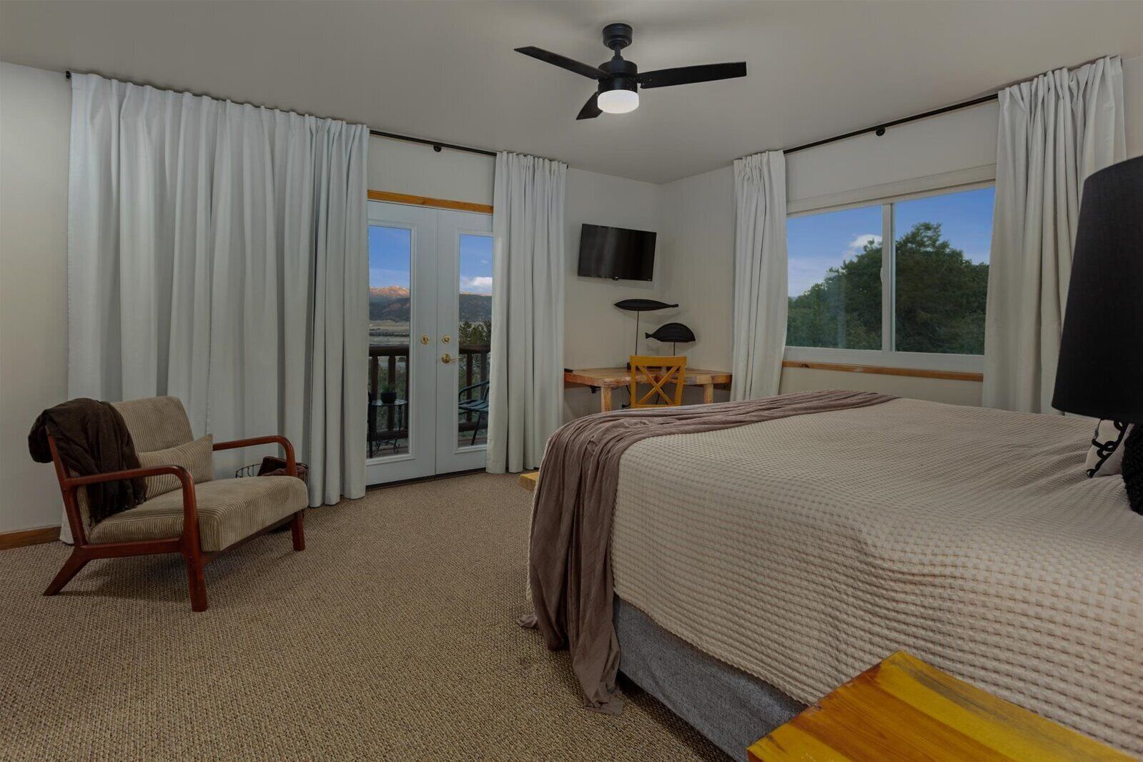 A hotel room with a bed, a chair, a desk, a ceiling fan, and a TV.