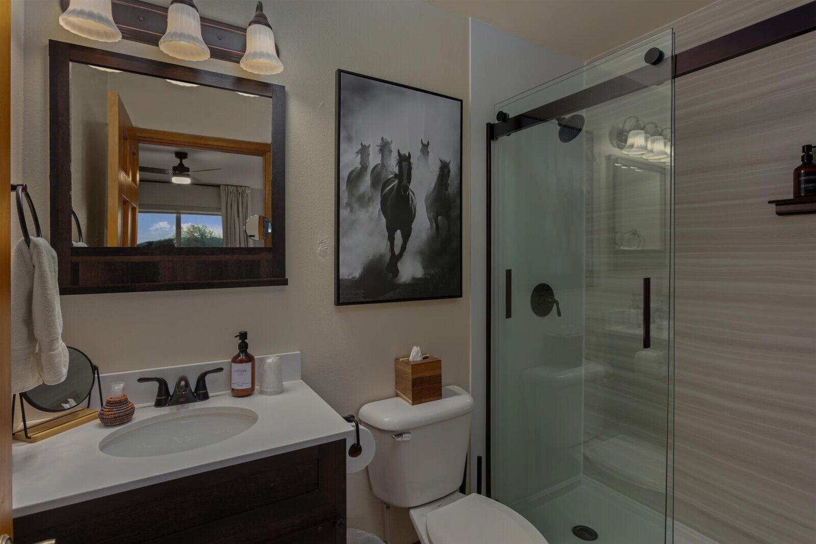 A bathroom with a glass shower enclosure, a sink with a mirror, and a toilet.