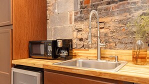 Une cuisine compacte équipée d’un four à micro-ondes encastré, d’une machine à café et d’un évier en acier inoxydable.