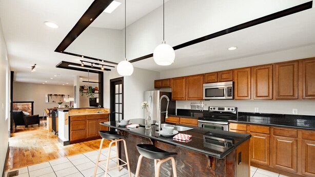 Une cuisine moderne avec des meubles en bois, un îlot central doté de tabourets, un four à micro-ondes, une cuisinière et une grande fenêtre.