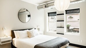 Une chambre moderne avec un grand lit, un miroir rond, une table de chevet avec une lampe et une fenêtre donnant sur l’extérieur.