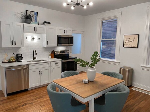 A modern kitchen with white cabinets, stainless steel appliances, and a wooden dining table with two chairs.