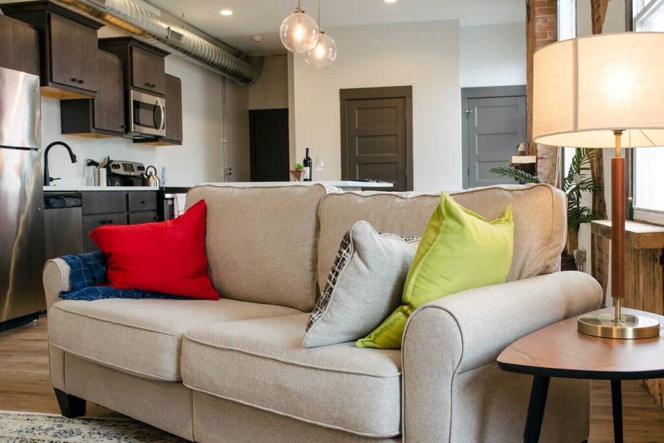 A living room with a beige sofa, a round wooden side table, and a lamp.