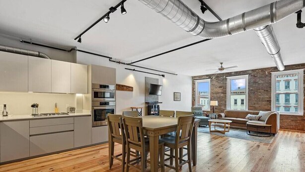 A modern kitchen with a dining area, wooden flooring, and large windows. - Findlay Suites - Perfect Location Over the Rhine (Cincinnati)