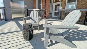 A covered outdoor deck with Adirondack chairs, a round table, and a decorative vase. - Findlay Suites - Perfect Location Over the Rhine (Cincinnati)