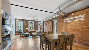 A spacious kitchen with wooden flooring, a dining area with a wooden table and chairs, and a brick wall. - Findlay Suites - Perfect Location Over the Rhine (Cincinnati)