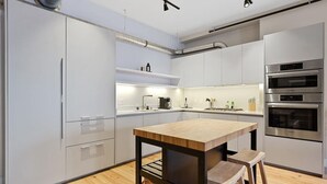 Una cocina moderna con armarios blancos, electrodomésticos de acero inoxidable, una isla de madera y taburetes.