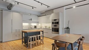 Una cocina moderna con una isla central, taburetes de madera y una mesa de comedor con sillas.