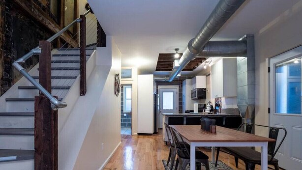 Eine moderne Küche mit einer zentralen Kochinsel, einem Essbereich mit einem Holztisch und Stühlen sowie einer Treppe mit Metallgeländern.