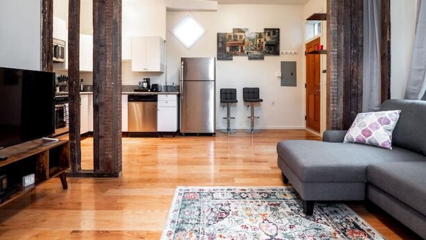 A modern living room with a grey sofa, a TV, and a patterned rug. - Cozy OTR Home with Private Roof Deck (Cincinnati)