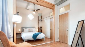 A modern bedroom with a wooden floor, a bed with white bedding, a blue throw blanket, a standing lamp, and a ceiling fan. - Cozy OTR Home with Private Roof Deck (Cincinnati)