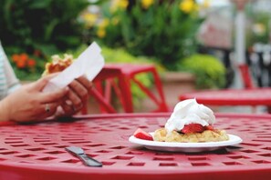 Een dessert op een bord, met slagroom en een aardbei op een rode tafel.