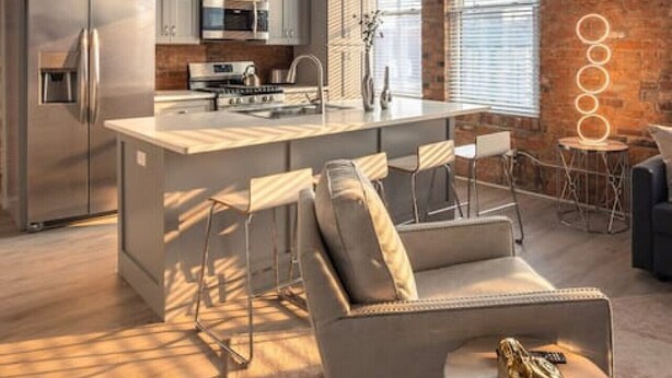 A modern kitchen with a central island, bar stools, and a seating area with a sofa and a small table.