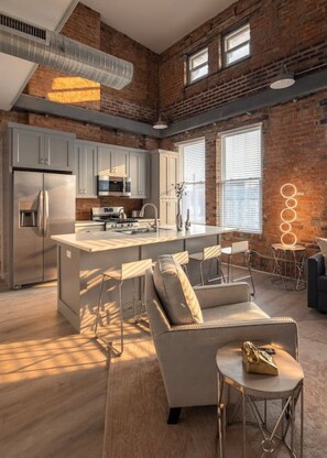 A modern kitchen with a central island, bar stools, and a seating area with a sofa and a small table. - Bubbles · BUBBLES FANTASY SUITE: Explore OTR/DT & Rhinegeist (Cincinnati)