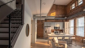 A modern kitchen with a central island, a dining area with bar stools, and a staircase with a metal railing. - Entire Historic Building: Sleeps 30 (Cincinnati)