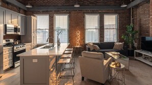 A spacious kitchen with a central island, a dining area with bar stools, a sofa, and a TV. - Entire Historic Building: Sleeps 30 (Cincinnati)