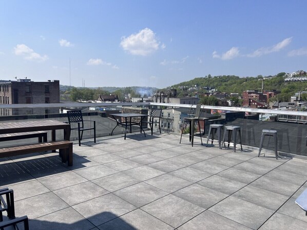 A rooftop terrace with tiled flooring, metal furniture, and a view of a cityscape.