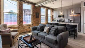 A modern living room with a grey sofa, a coffee table, and a dining area with a kitchen in the background.