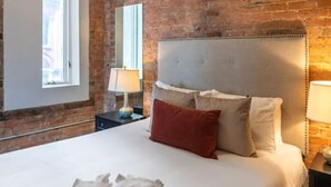 A bedroom with a brick wall, a bed with white bedding, a ceiling fan, and a window.