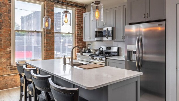 A modern kitchen with a central island, stainless steel appliances, and exposed brick walls.