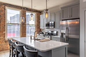 A modern kitchen with a central island, stainless steel appliances, and exposed brick walls.