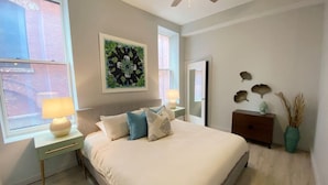 A bedroom with a bed, bedside tables, a ceiling fan, a window, and a wall-mounted artwork.