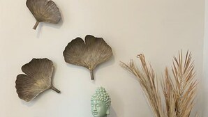 A wooden dresser with a single drawer, a green vase with dried plants, and three wall-mounted decorative leaves.