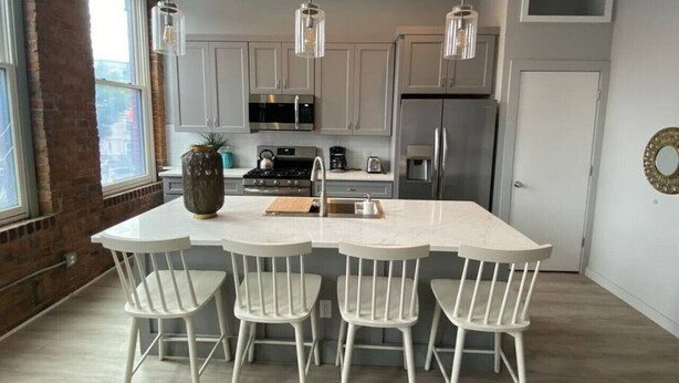 A modern kitchen with white cabinets, a central island with bar stools, stainless steel appliances, and pendant lighting.