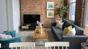 A living room with a brick wall, a flat-screen TV, a sofa, a coffee table, and a potted plant.