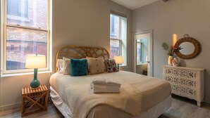 A neatly arranged bedroom with a large bed, two bedside tables, a dresser, and a mirror.