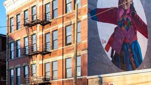 Un edificio con un gran mural en la fachada, escaleras de incendios y coches aparcados.